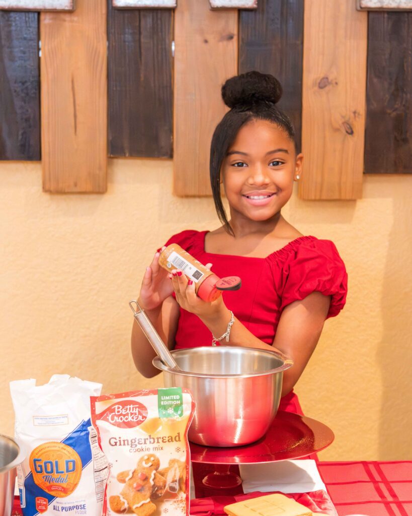 Little girl in red dress holding cinnamon jar while baking.