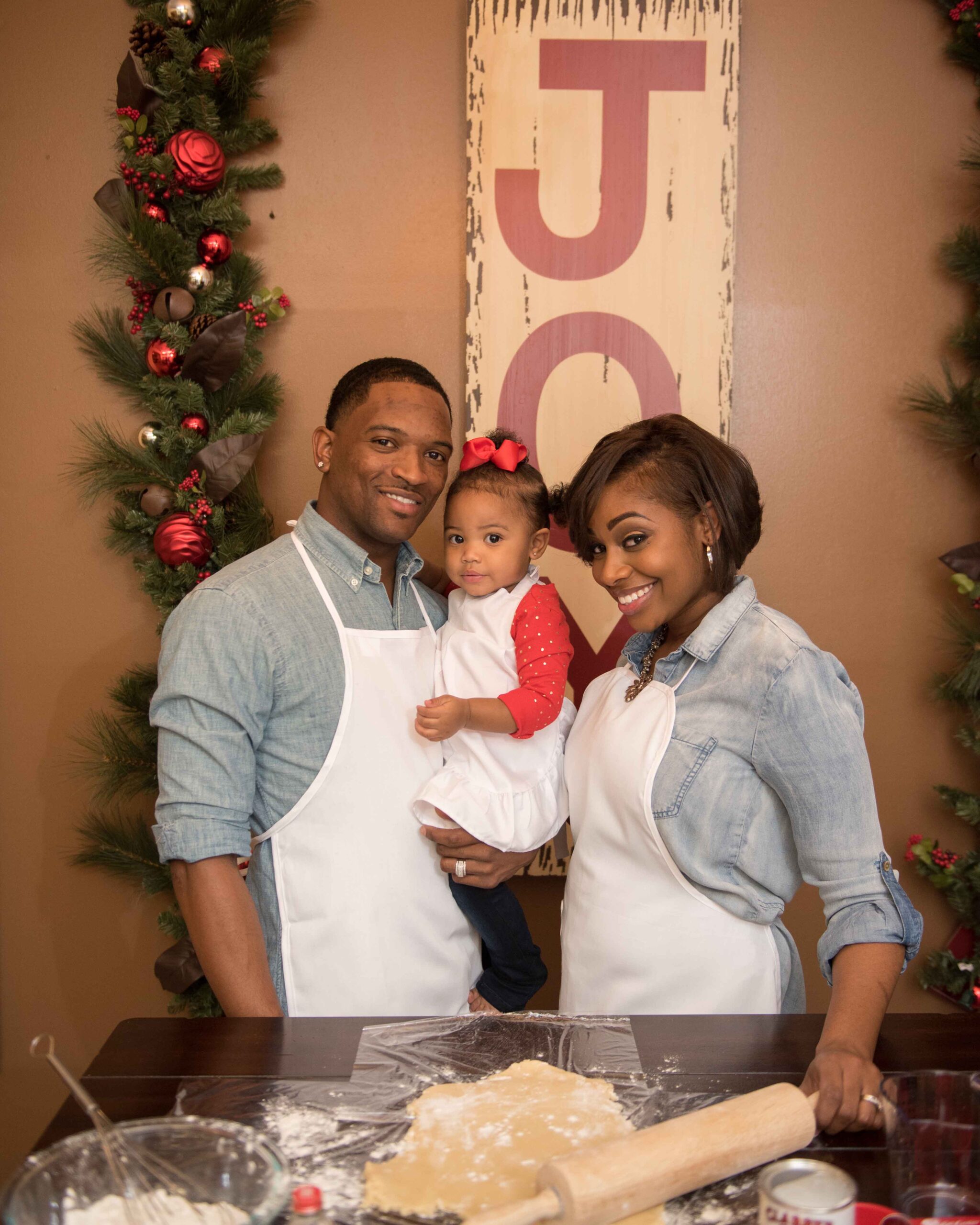 Young family with baby girl in matching aprons surrounded by Christmas décor.