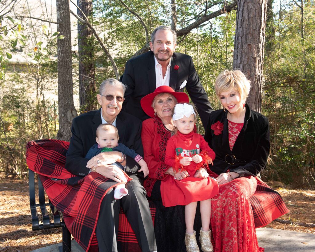 Extended family spanning three generations smiling outdoors in festive red and black attire
