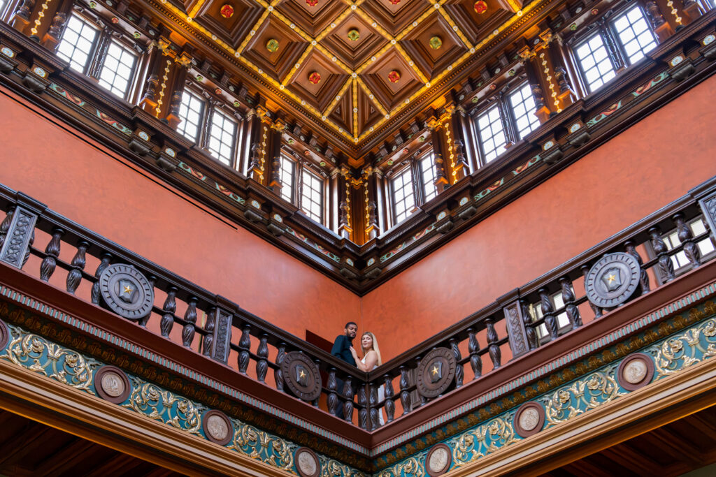 Julia Ideson Library engagement photography featuring an elegant couple on the historic balcony under the ornate patterned ceiling